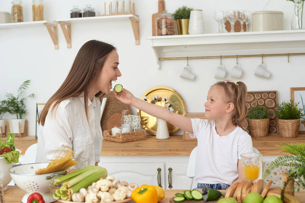 Máma a dcera jedí okurky a smějí se. Správná výživa doma. Trávit čas společně - Fotografie, Obrázek