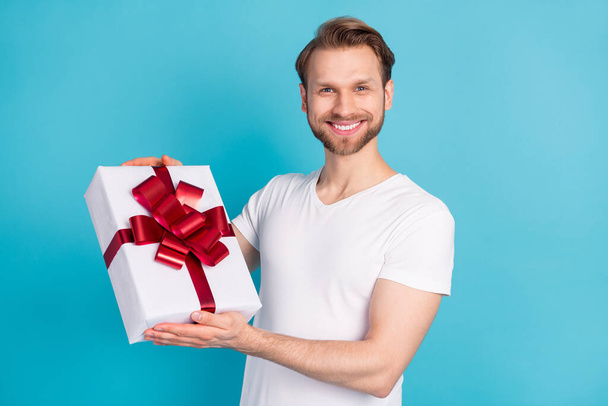 Portrait of cheerful man arms holding giftbox look camera beaming smile isolated on blue color background - Zdjęcie, obraz
