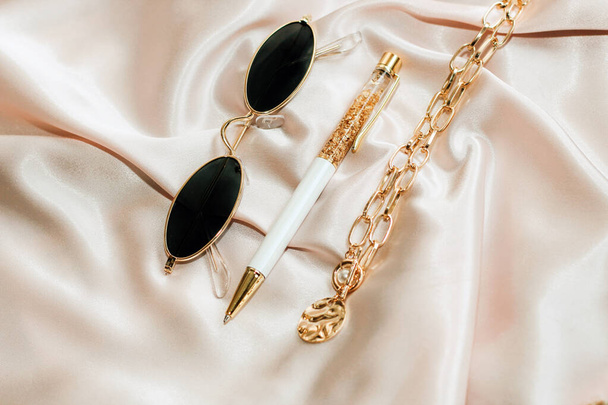 Sunglasses in a gold frame with a handle and a chain on a silk background. Flatley. - Foto, afbeelding