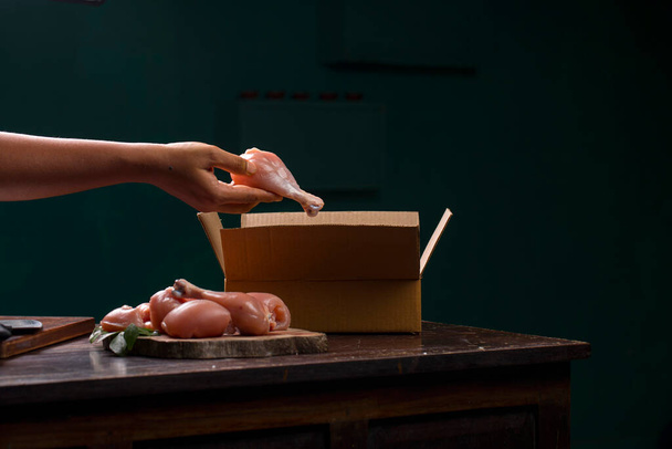 Rohe Hühnerschnitte oder Teile ohne Haut, die auf einem aufgeschnittenen Holzbalken angeordnet sind, und ein Arbeiter, der rohes Huhn für die Lieferung verpackt, das auf einem Holzuntergrund platziert ist. - Foto, Bild
