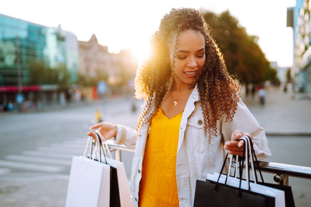Νεαρή γυναίκα με τσάντες για ψώνια που περπατάει στο δρόμο. Πώληση, ψώνια, τουρισμός και ευτυχισμένοι άνθρωποι έννοια.  - Φωτογραφία, εικόνα