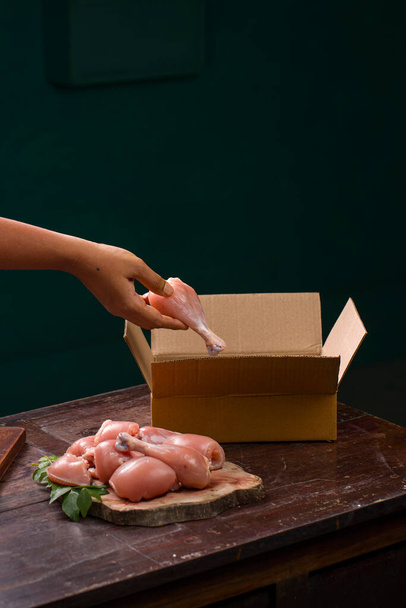 Morceaux ou parties de poulet cru sans peau disposés sur une base en bois tranché et un ouvrier emballant du poulet cru pour la livraison qui est placé sur un fond en bois. - Photo, image