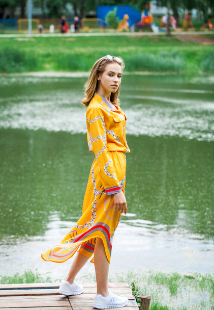 Full body portrait of a young beautiful blonde girl in golden dress posing by the lake - Foto, immagini