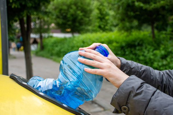 A close-up photo of a lady throwing away the plastic bottle in a container for sorting out the trash. The photo can be used as an illustration dedicated to topics of saving the environment in the articles or websites - Photo, Image