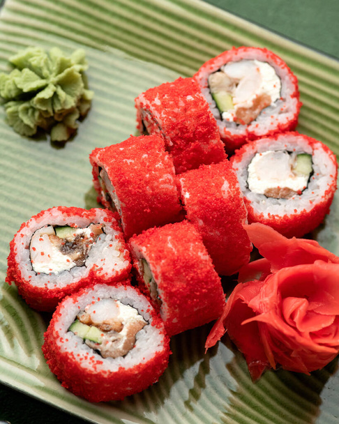 Red Sushi roll in masago or tobiko caviar on green background. Inside-out Sushi Set. Red on green, Bright colors. Japanese food, Oriental cuisine. Close up shot. Top view. Soft focus - Photo, Image