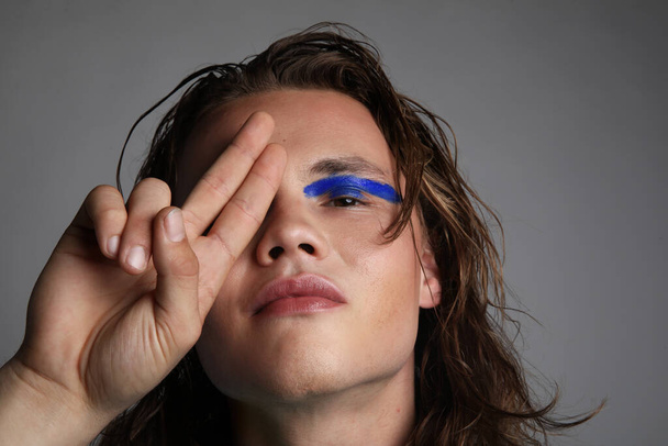 Young caucasian guy with creative make-up posing in the studio. - Foto, afbeelding