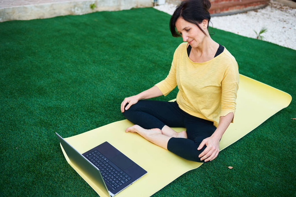 Een vrouw neemt een yoga klas van haar laptop buiten - Foto, afbeelding