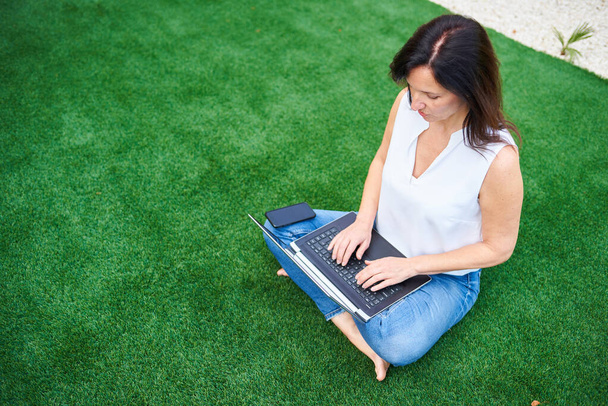 A Caucasian brunette woman uses her laptop in the garden of her house it is daytime there is natural light - Photo, Image