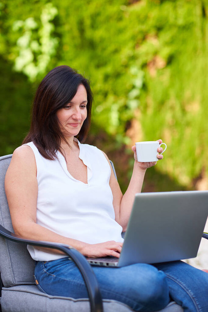 Biała brunetka trzyma filiżankę kawy podczas pracy na laptopie - Zdjęcie, obraz