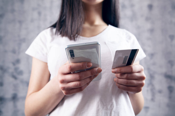 woman makes a payment by phone through a card on a gray background - Foto, Bild