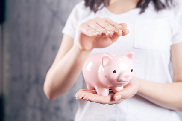 young woman holding a piggy bank in her hands on a gray background - Foto, immagini