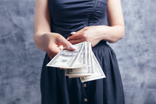 young woman gives money on gray background - Φωτογραφία, εικόνα