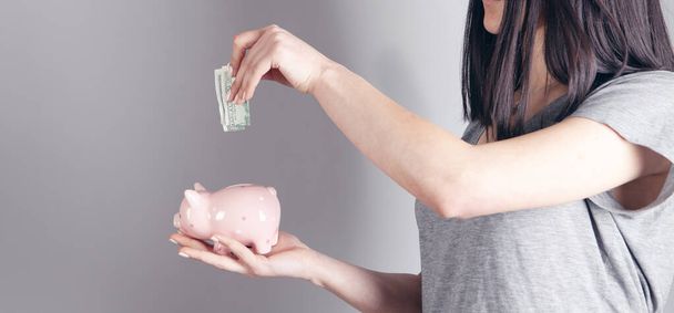 young woman throws dollar into piggy bank on gray background - Fotografie, Obrázek