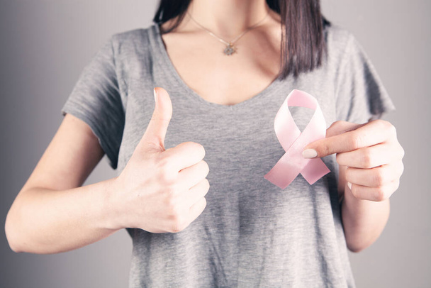 young girl holding pink ribbon and showing thumb up on gray background - Fotoğraf, Görsel