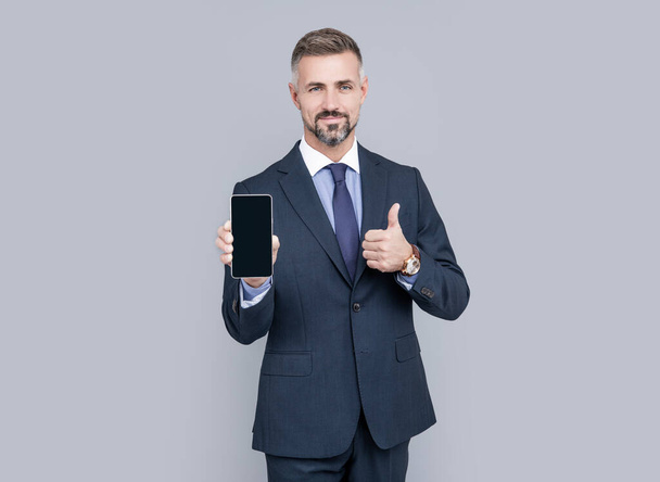 mature man influencer in suit presenting mobile phone device and show thumb up, best offer. - Фото, изображение