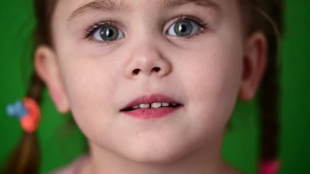 Klein meisje knipperende ogen, slow motion van een kind, portret op een groene achtergrond. - Video