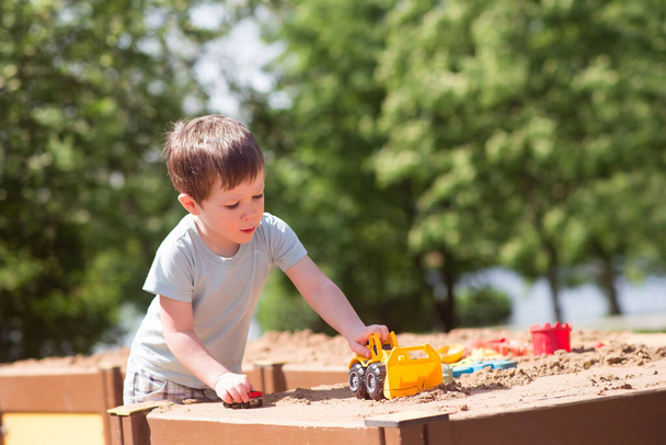 Um menino brinca com brinquedos, carros na areia no parque infantil. Jardim de infância - Foto, Imagem