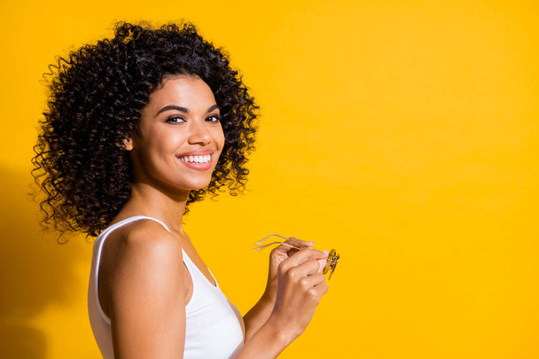Profile photo of adorable satisfied dark skin lady hands hold sunglass isolated on yellow color background - Foto, Imagem