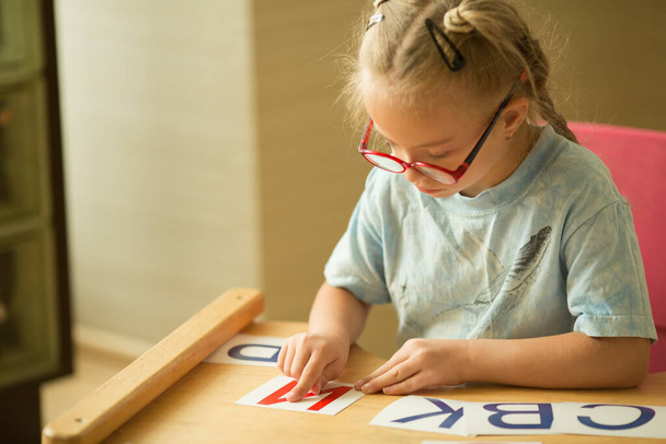 Ένα κορίτσι με σύνδρομο Ντάουν μελετά το αλφάβητο. - Φωτογραφία, εικόνα