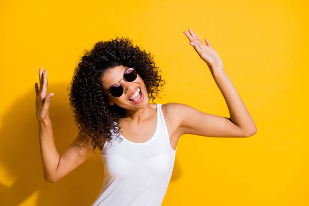Photo of cheerful dark skin girl dance cool wear summer outfit raise hands isolated on funky yellow color background - Фото, изображение