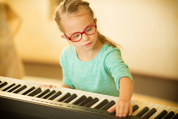 Ένα κορίτσι με σύνδρομο Down μαθαίνει να παίζει πιάνο. - Φωτογραφία, εικόνα