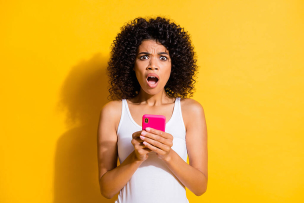 Photo of scared amazed brunette afro american woman hold phone wear white tank-top isolated on yellow color background - Фото, изображение