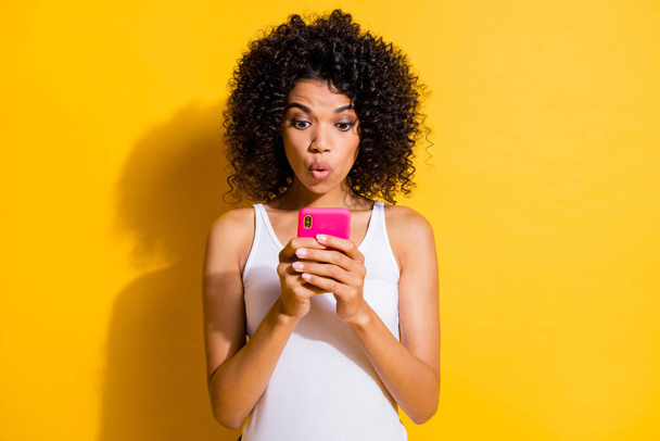 Photo of impressed cute young dark skin lady wear white singlet typing modern device isolated yellow color background - Foto, Bild