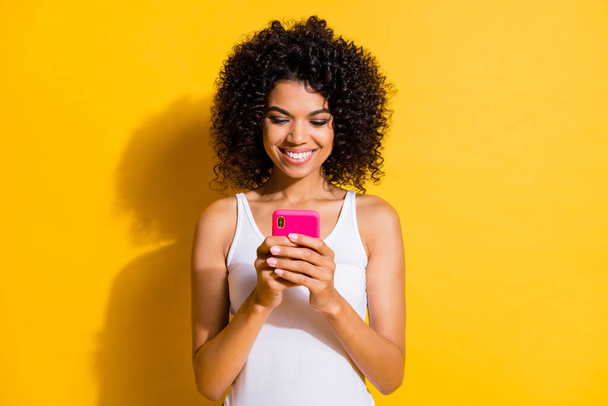 Photo of charming cheerful dark skin girl hands hold phone typing blog post isolated on yellow color background - Zdjęcie, obraz