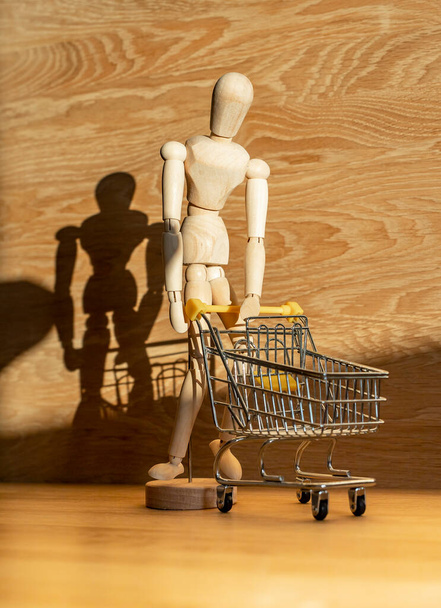 Burden of shopping concept, crisis. Wood man bent and leaning over shop cart in beautiful day light - 写真・画像