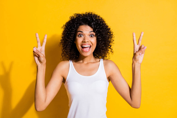 Portrait of excited positive dark skin open mouth two arms fingers show v-sign isolated on yellow color background - Φωτογραφία, εικόνα