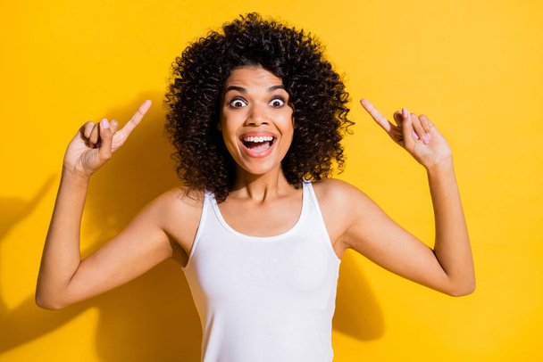 Photo of excited funny young dark skin woman dressed white tank-top pointing up empty space isolated yellow color background - Fotó, kép