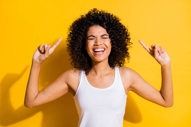 Photo of laughing pretty young dark skin lady wear white singlet closed eyes pointing up empty space isolated yellow color background - Foto, afbeelding