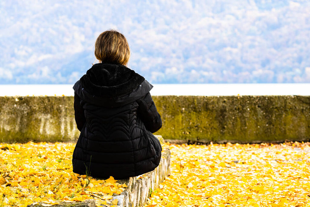 Des feuilles d'automne tombées sur une femme seule dans la ruelle d'automne. Paysage d'automne, feuillage d'orange dans un parc à Orsova, Roumanie, 2020 - Photo, image