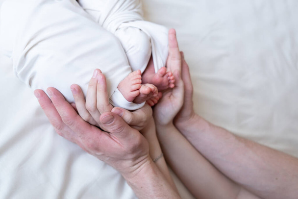 Mom and dad hands hold small legs of their two newborn twin babies - Photo, Image