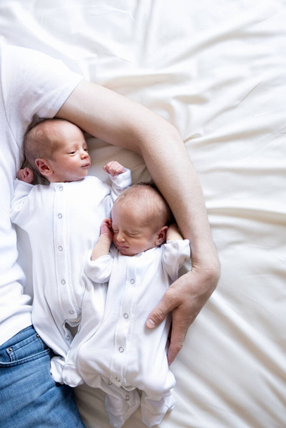 Gémeos idênticos recém-nascidos na cama, nas mãos dos pais. Estilo de vida, emoções de crianças. Bebês infantis com espaço de cópia - Foto, Imagem