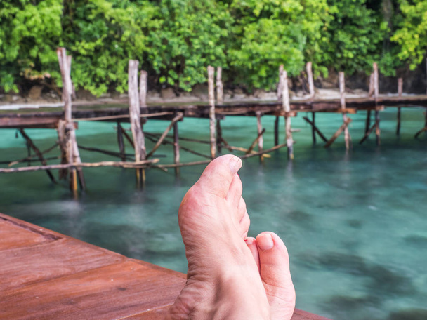 Relax over the turquoise water. Woman feet on the wooden pond. - Photo, image