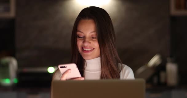Houkutteleva nuori nainen freelancer käyttää älypuhelinta tietokoneella ja katsoo monitoria. Muotokuva naisesta työstämässä läppäriä. Etätyö freelancer kotona. - Materiaali, video