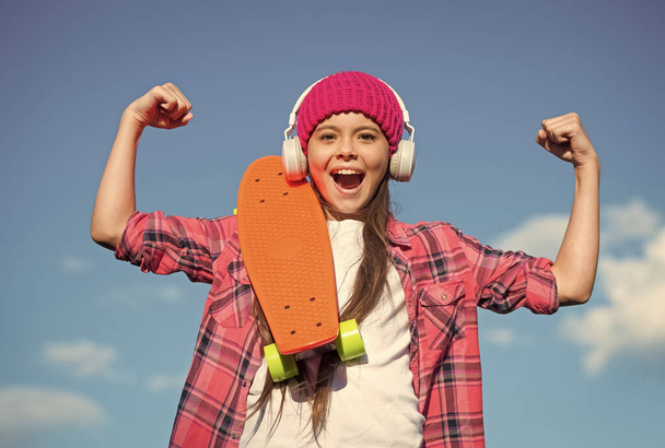 Girl power. Happy skater flex arms on blue sky. Little child with penny board outdoors. Power slide trick. Friction playground . Energy skate park. Power of skateboarding. Fun physics activities - Foto, Bild