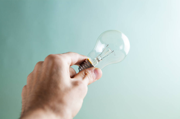 hand holding a light bulb on a blue background - Zdjęcie, obraz