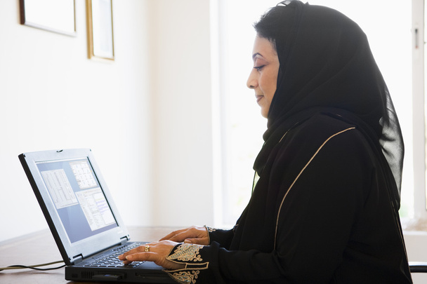 A Middle Eastern woman sitting in front of a computer at home - Φωτογραφία, εικόνα