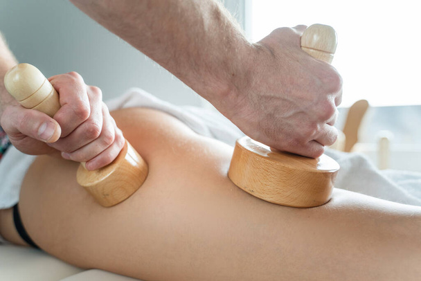 Nahaufnahme auf dem Rücken einer unbekannten Frau bei einer Maderotherapie-Massage gegen Cellulite durch einen professionellen Therapeuten, der im Studio oder Salon mit Kopierraum Holzwerkzeuge in den Händen hält - Foto, Bild