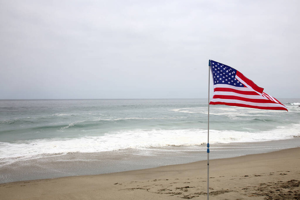 アメリカ独立記念日。7月4日。アメリカ独立記念日。アメリカ国旗だ。7月4日。アメリカ独立記念日。アメリカのビーチで砂の中のアメリカ国旗。アメリカは自由と生活の質で第一位です. - 写真・画像