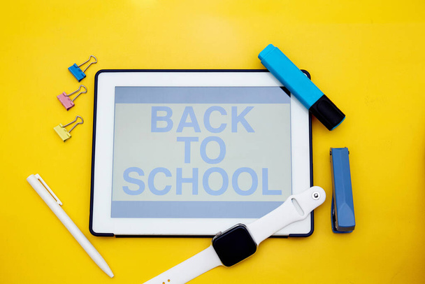 Okul konseptine geri dönelim. Okula Dönüş metniyle dijital tablet ekranının üst görüntüsü. Akıllı saat ve okul malzemeleri sarı üzerine izole edilmiş.  - Fotoğraf, Görsel