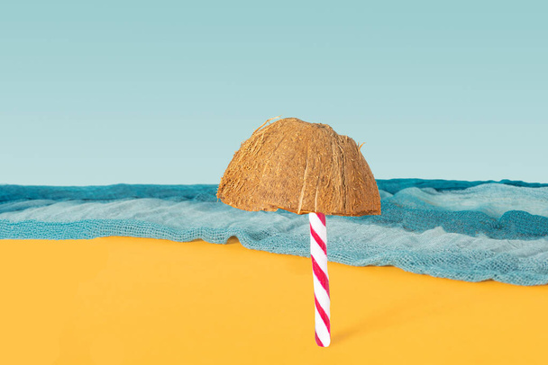 Пляж з самотньою сонячною парасолькою абстрактна концепція. Цукеркова тростина і половина свіжого сирого органічного кокосового горіха спереду з блакитним океанським шарфом і блакитним фоном неба
. - Фото, зображення