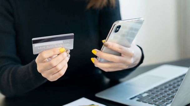 Młoda kobieta płaci kartą kredytową online dokonując zakupu online na laptopie. Skuteczni przedsiębiorcy dokonują transakcji przy użyciu mobilnej aplikacji bankowej. - Zdjęcie, obraz