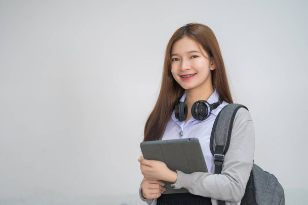 Porträt einer jungen asiatischen Studentin in Uniform, die ein Tablet in schicker und glücklicher Pose im Hörsaal der Universität oder Hochschule hält. Jugendschülerin und Nachhilfeunterricht mit technologischem Lernkonzept - Foto, Bild