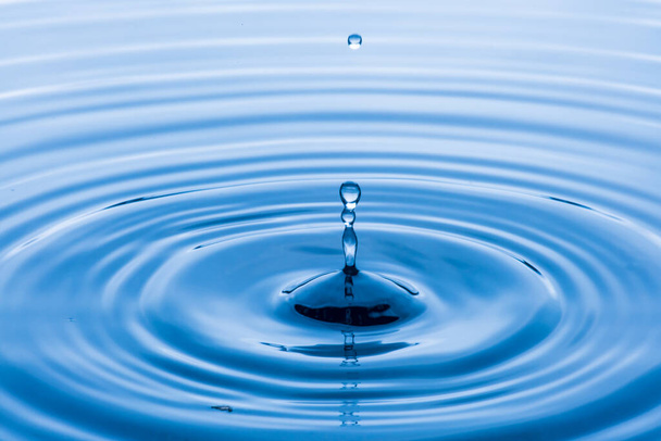 water drop splash in a glass blue colored shot of water that is dripping and reflecting water.soft focus. - 写真・画像