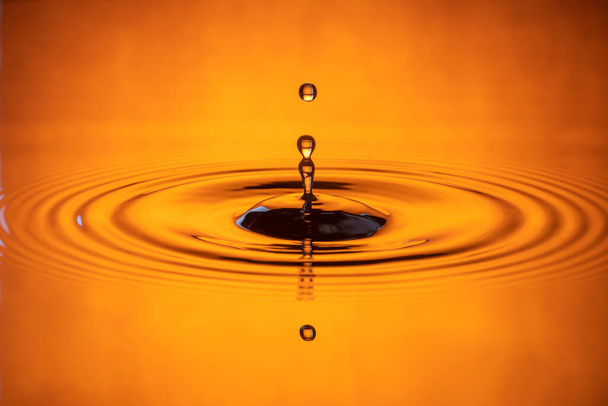 Wassertropfen plätschern in einem orangefarbenen Glas aus Wasser, das tropft und Wasser reflektiert. - Foto, Bild