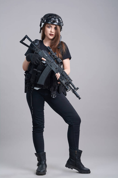 Une jeune femme avec une mitrailleuse dans les mains sur un fond gris - Photo, image