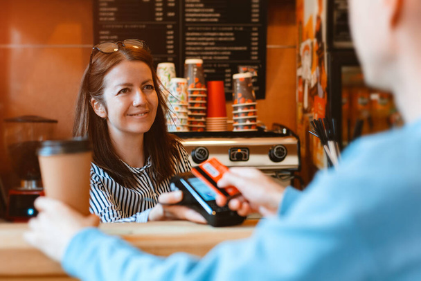 barista υποβάλλει ένα τερματικό για μη χρηματική πληρωμή. Πελάτης πληρώνει το λογαριασμό μέσω κάρτας χρησιμοποιώντας την τεχνολογία NFC στο καφέ - Φωτογραφία, εικόνα